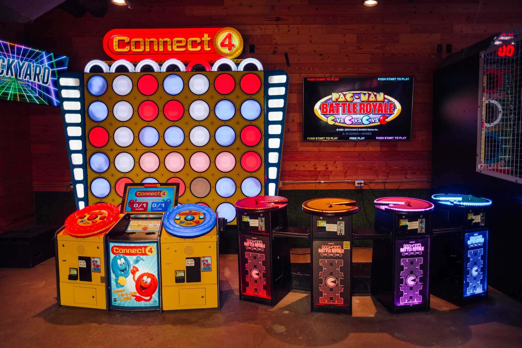 Colorful arcade setup featuring oversized Connect 4 and Pac-Man Battle Royale games at an indoor entertainment venue.