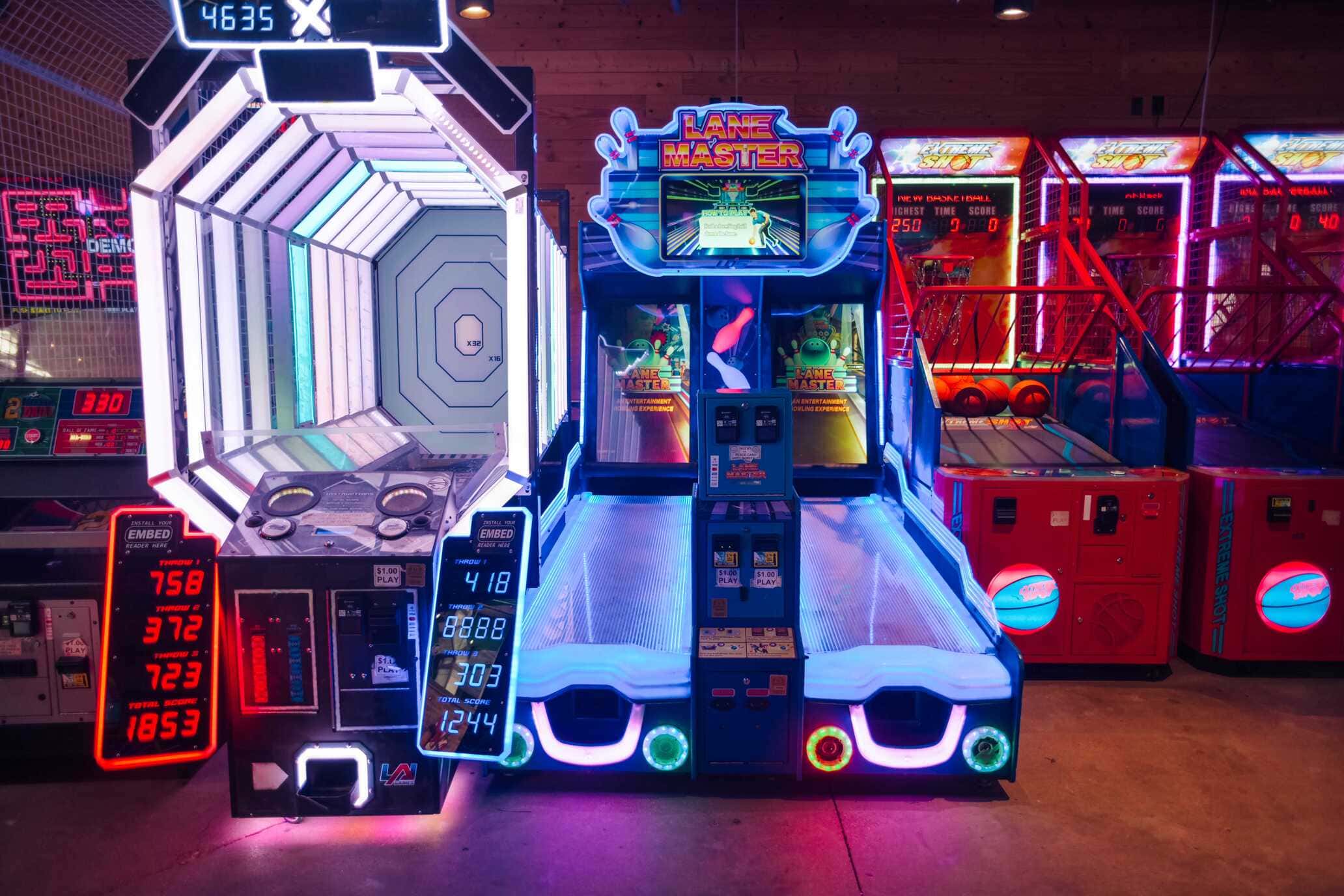 Neon-lit arcade area featuring basketball shootout, Lane Master bowling game, and futuristic tunnel game at Backyard Dallas